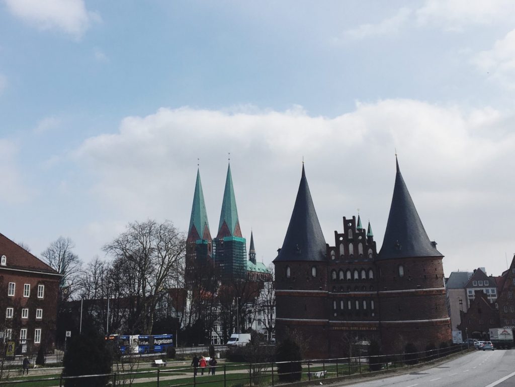 Das Lübecker Holstentor im Sonnenschein. Zu sehen sind die beiden Türme des Tors und die zwei Türme des Lübecker Doms.