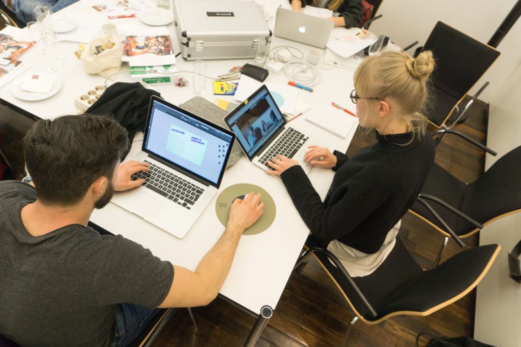 Man sieht zwei junge Menschen die mit Laptops über Eck an einem Schreibtisch sitzen und für ein Projekt der Nachtschicht arbeiten.