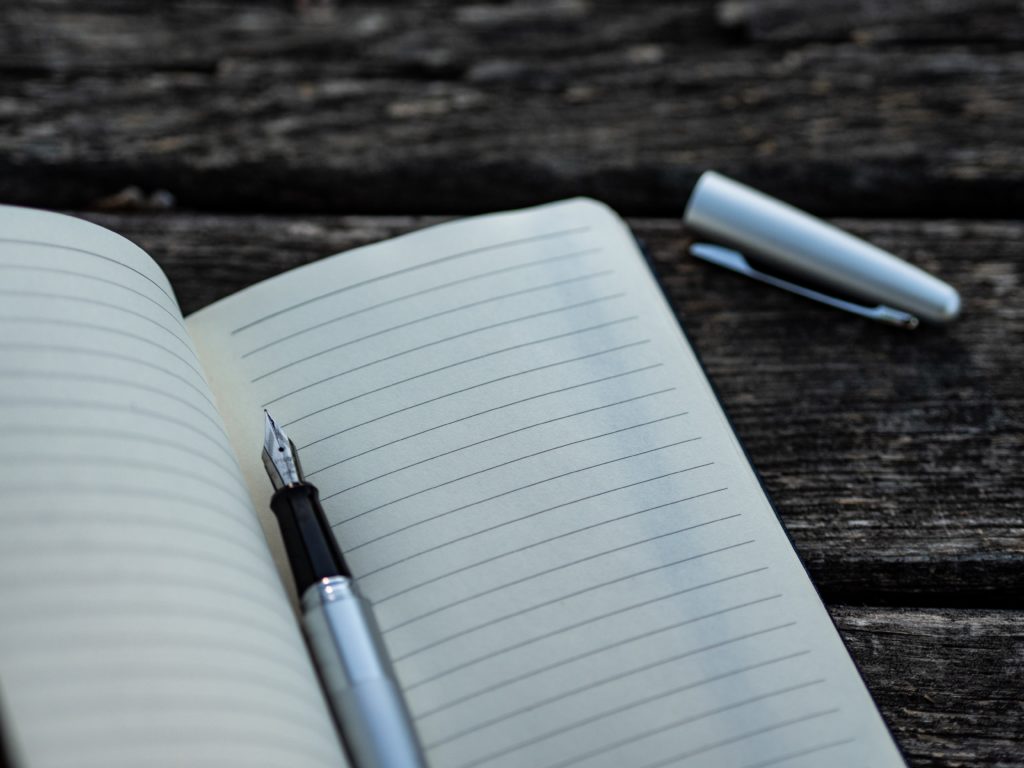 Ein aufgeschlagenes Notizbuch mit leeren Seiten liegt auf einem Tisch, in ihm liegt ein Füller ohne Deckel.