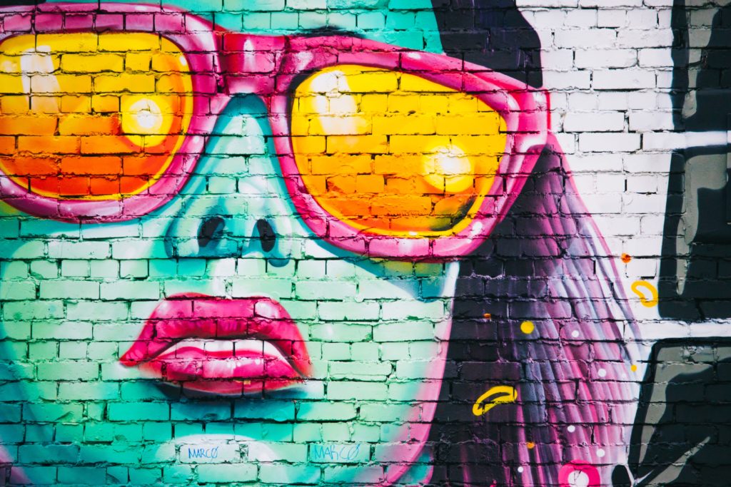 Graffiti auf einer weissen Mauer zeigt eine Nahaufnahme einer Frau in Neonfarben