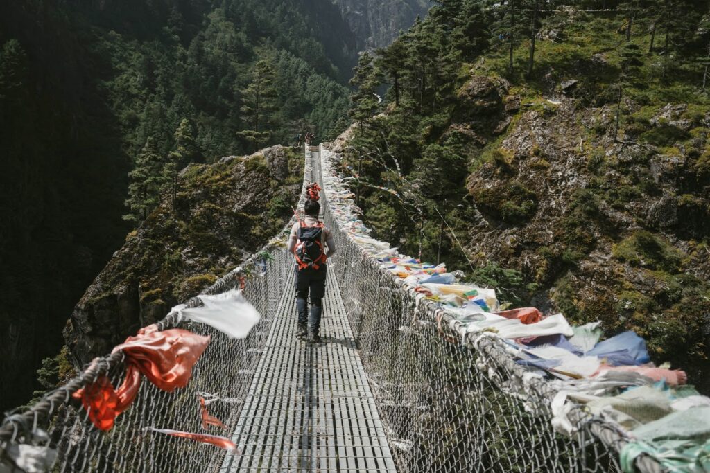 Ein Mann geht über ine mit Tüten behängte lange Hängebrücke mitten in der Natur, vermutlich China.