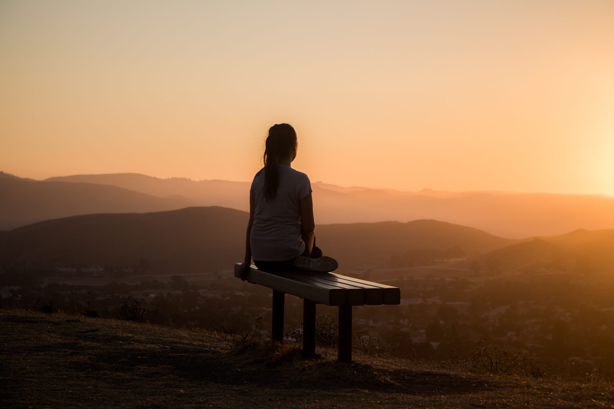 Frau meditiert im Sonnenaufgang auf einer Bank auf einem Berg, Blick ins Tal