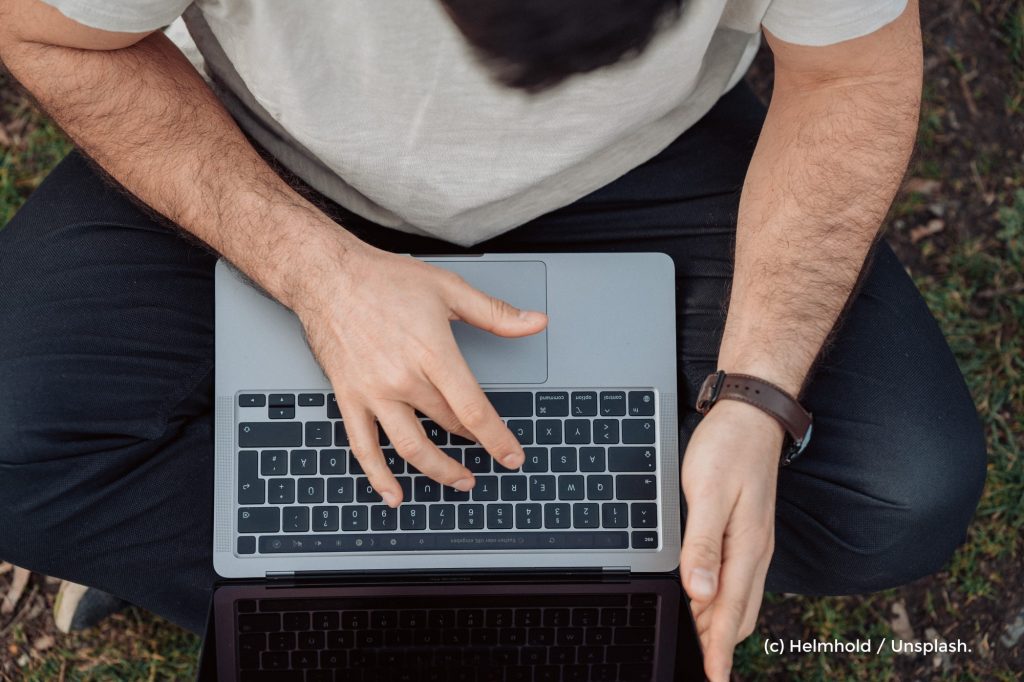 Foto eines Mannes, der in der Natur sitzt in digital per Laptop arbeitet. Symbolbild für das Pfingstcamp der Naturfreundejugend.