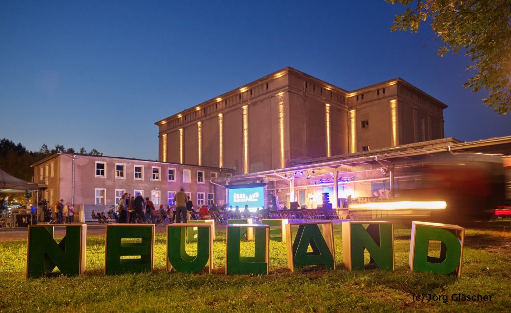 Foto vom Überland-Festival in Görlitz des Neuland gewinnen e.V. Im Hintergrund ist ein großes Steingebäude zu sehen, im Vordergrund der Schriftzug "Neuland".