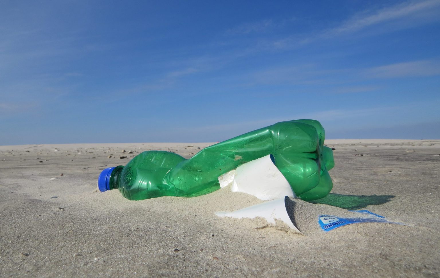 Eine leere Plastikflasche am Sandstrand, Sinnbild der ReplacePlastik App