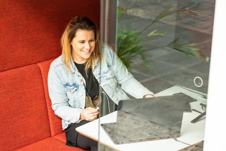 Insa Heinemann von der Braunschweigischen Stiftung sitzt in einer rotgepolsterten Telefonkabine in einem Coworkingspace und lächelt, während sie den Bildschirm anschaut.
