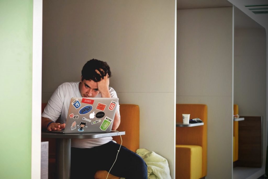 Foto: Ein Mann sitzt vor einem mit Stickern beklebten Laptop und rauft sich die Haare.
