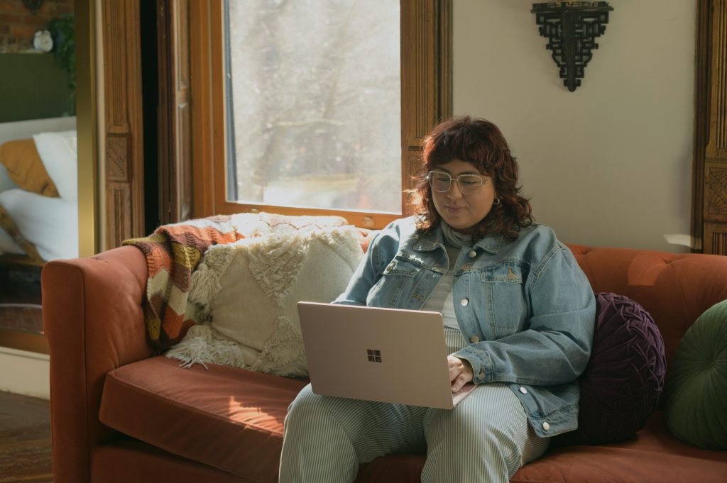Eine Frau sitzt am Laptop auf ihrem Sofa.