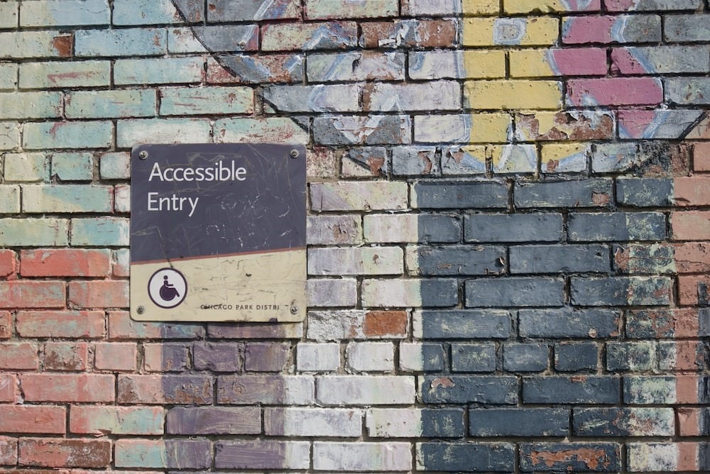 Bunte Backsteinwand mit Schild, auf dem "Accessible Entry" steht. Das Bild steht für Barrierefreiheit.