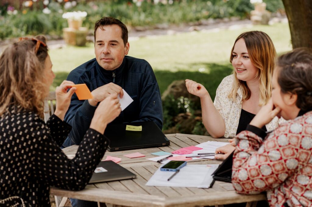 Vier junge Menschen sitzen in einem Garten an einem Tisch und planen mit Post-its etwas.
