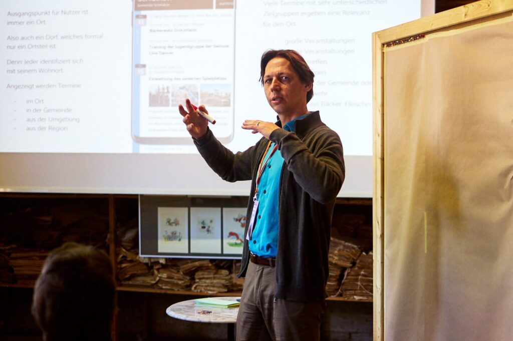 Person mit gehobenen Händen, vor einer Wand auf der eine Projektion einer Präsentation zu sehen ist.